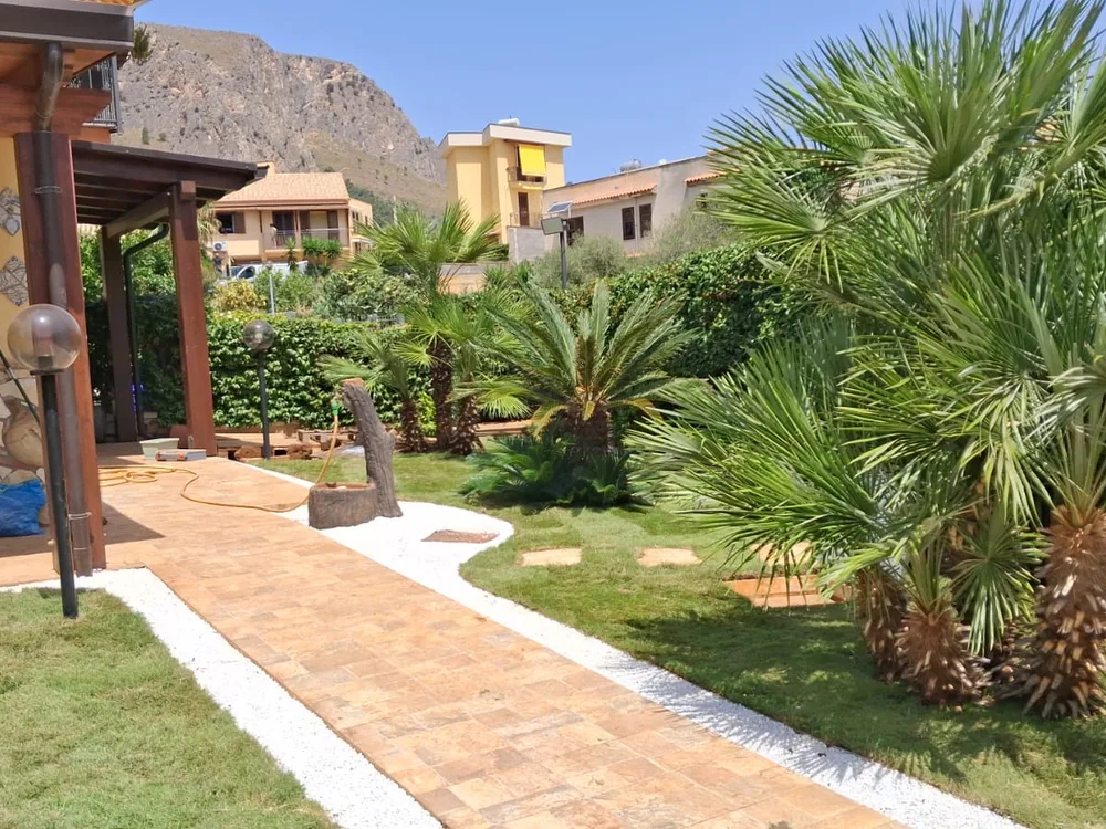 Vialetto in mattoni e ghiaia bianca fra il prato e la pergola della villa